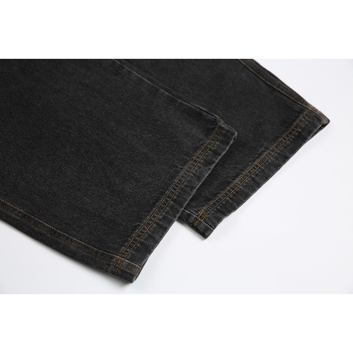Close-up of the hems of black denim jeans with double rows of orange-brown stitching.