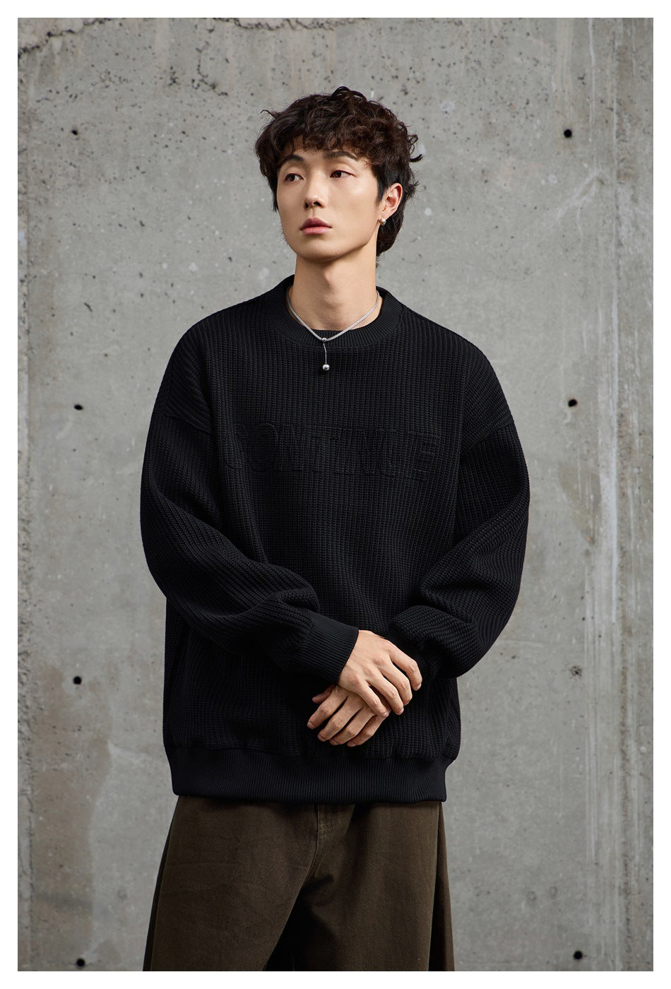 Closer front view of a model wearing an oversized black textured crewneck sweatshirt with subtle chest lettering.