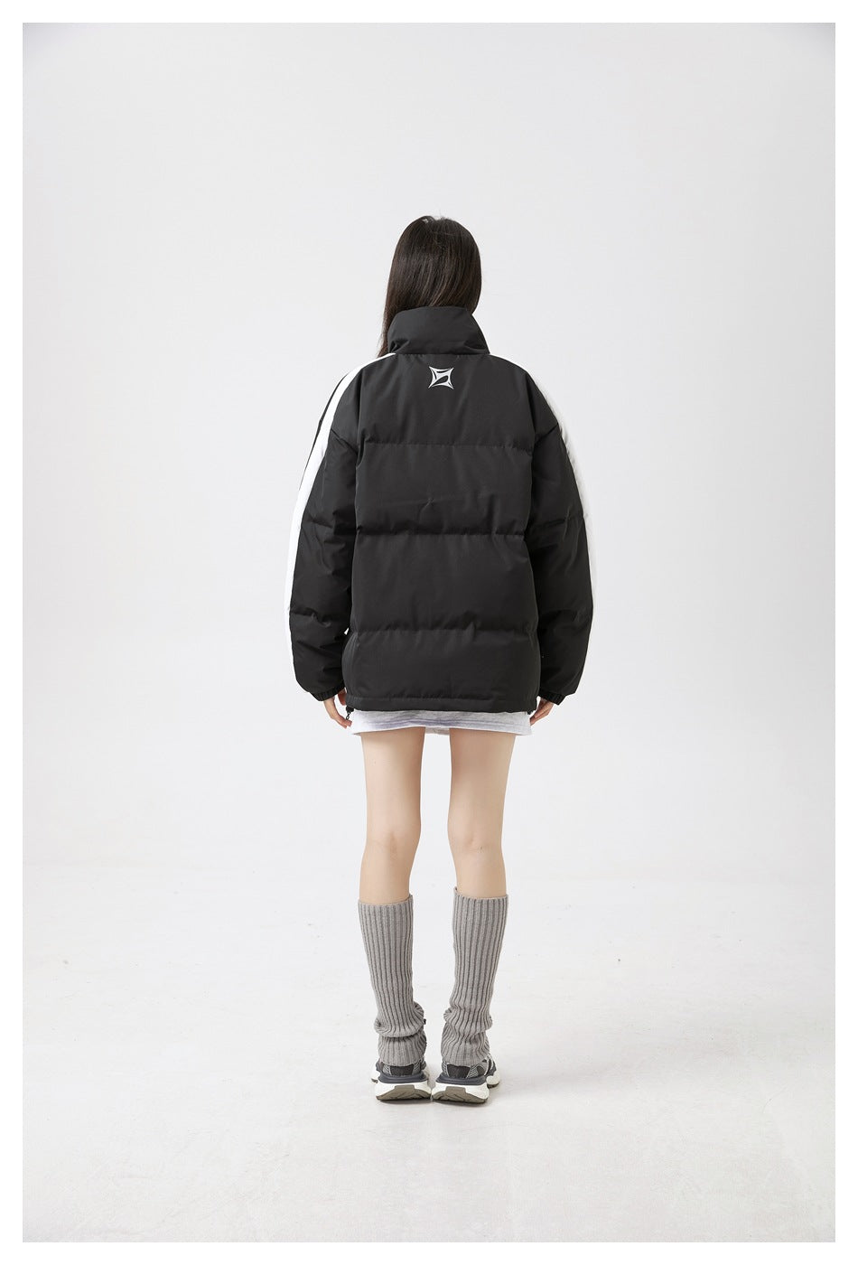Full back view of a model wearing a black padded jacket with white sleeve stripes and a small upper-back emblem.