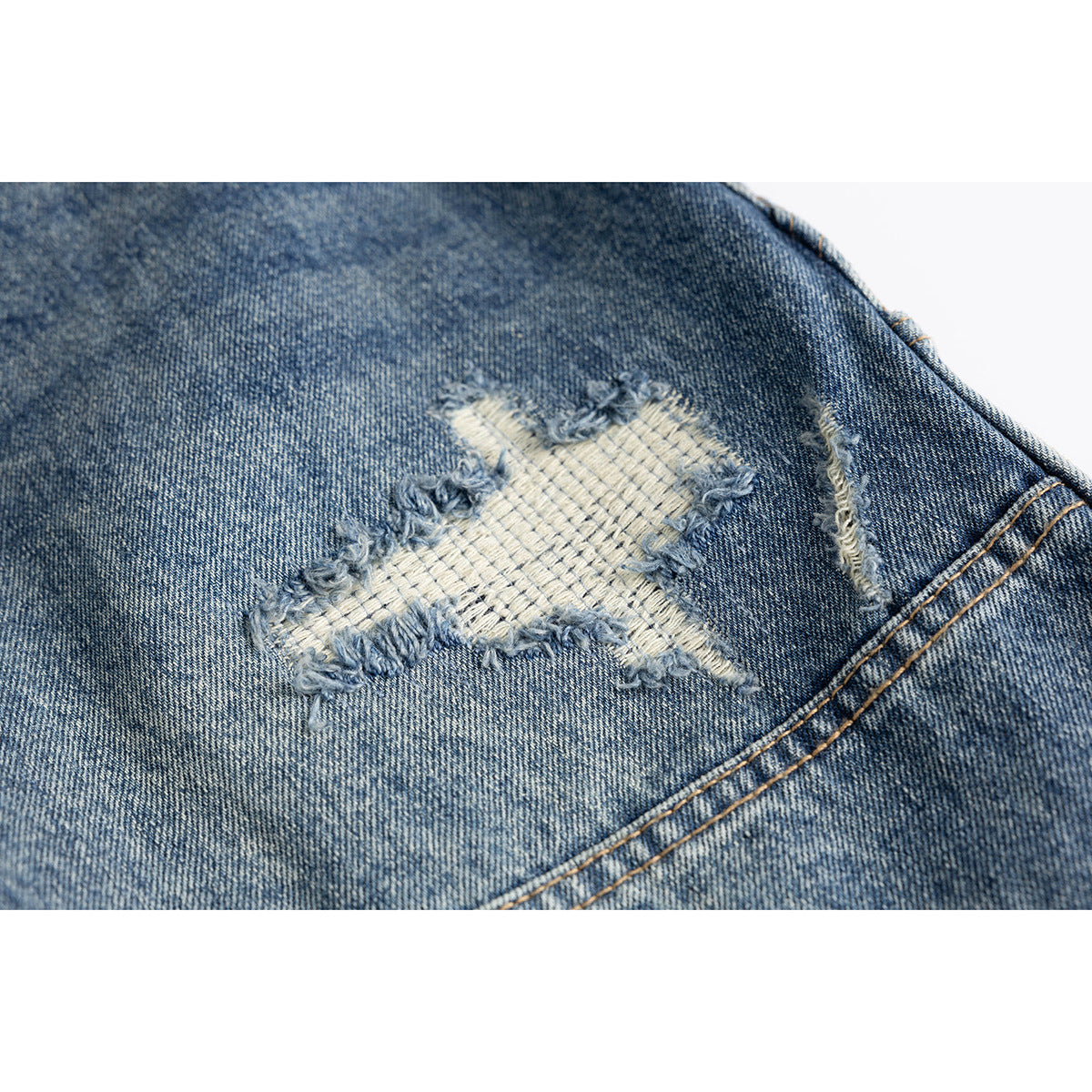 Close-up of a frayed, pale repair patch on blue denim, with distressed edges and nearby stitching.