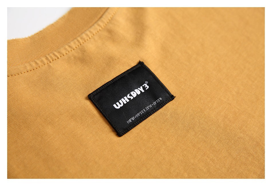 Close-up of a black woven label on the mustard T-shirt near the ribbed crew neckline.