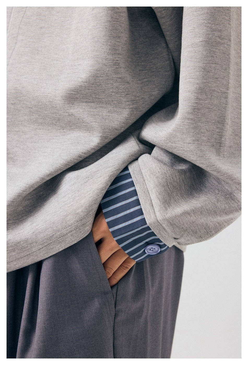 Close-up of the gray jacket sleeve and cuff over a blue striped shirt, with dark trousers visible.