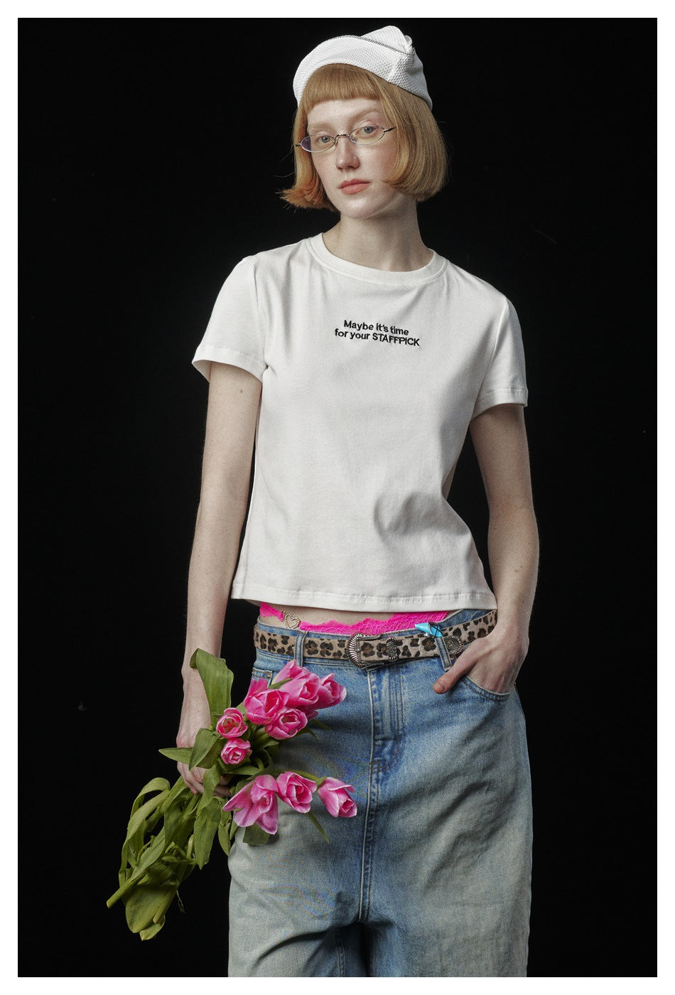 Closer view of a model wearing a white T-shirt with a small black English slogan and blue jeans, holding pink tulips.