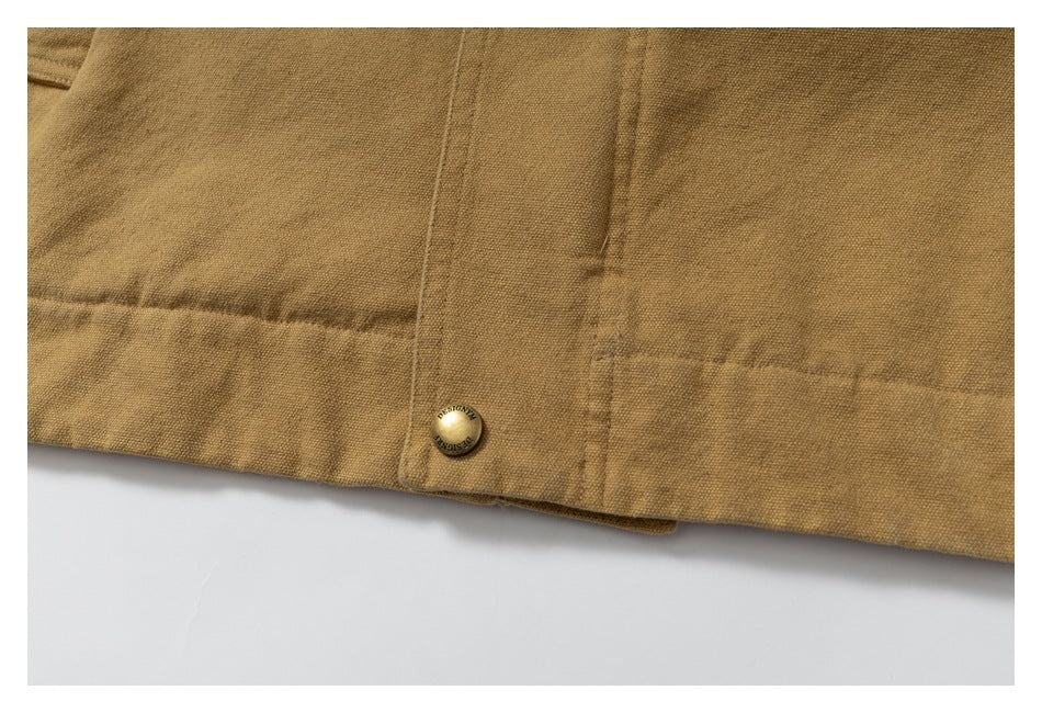 Close-up of the mustard-brown jacket hem, showing a stitched tab and a round metal snap button.