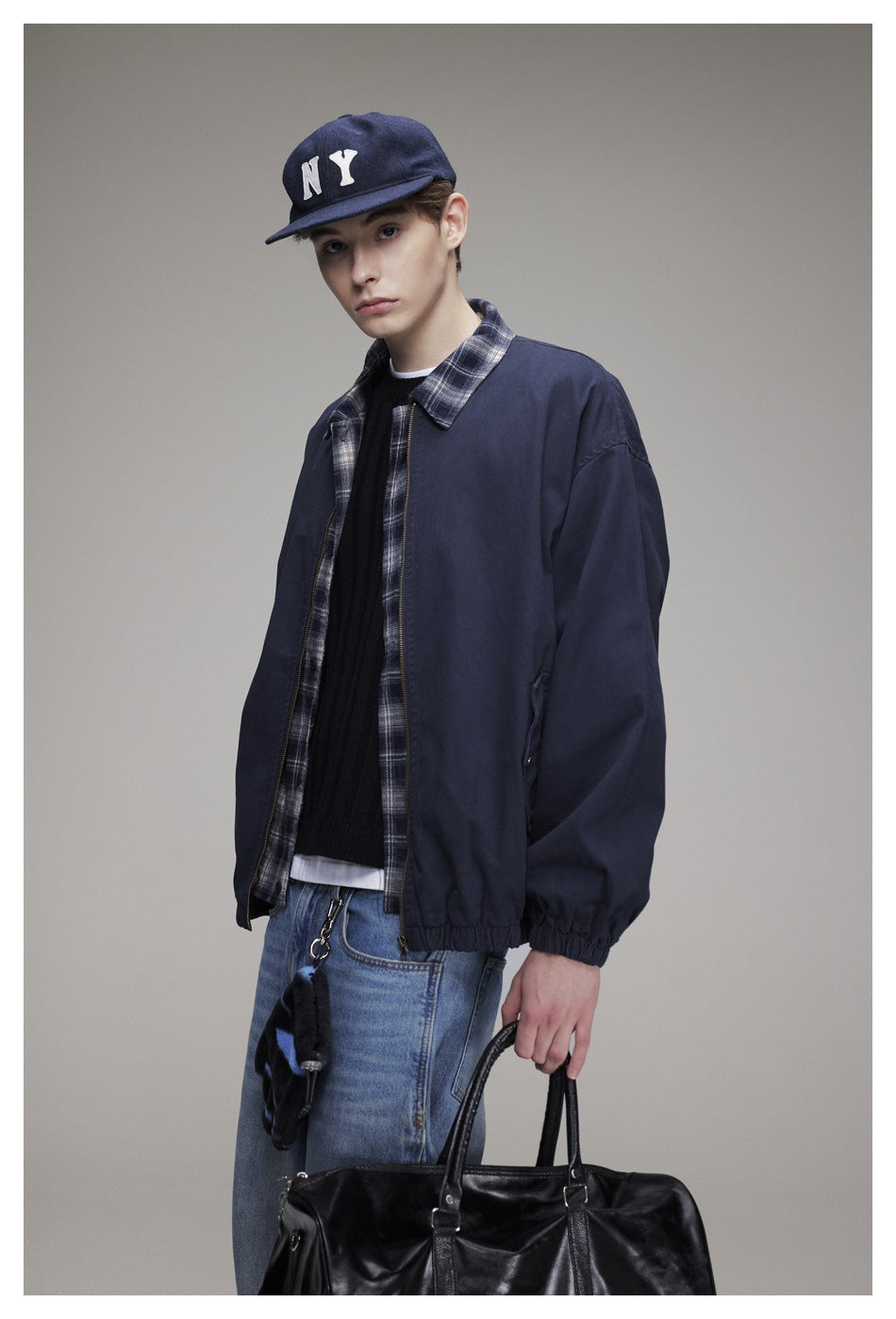 Three-quarter view of a model wearing an open navy jacket with plaid trim and elastic cuffs.