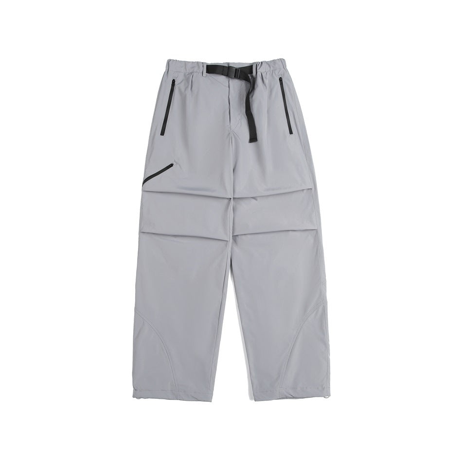 Front view of light gray loose-fit pants with a black waist belt, two zip pockets, and articulated panel seams.