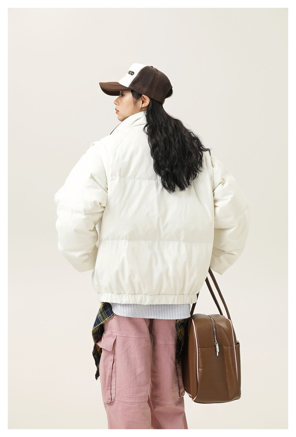 Model wearing the back of an ivory puffer jacket with a high collar and horizontal quilted panels.