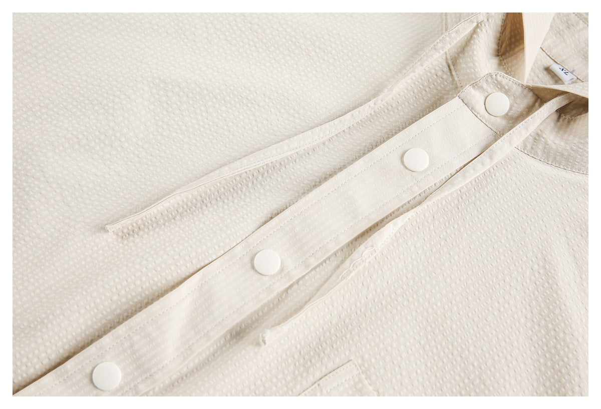 Close-up of the cream garment’s snap-button placket and stitched seams.