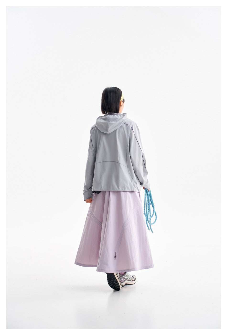 Rear view of a model wearing the light gray hooded jacket and lavender skirt.