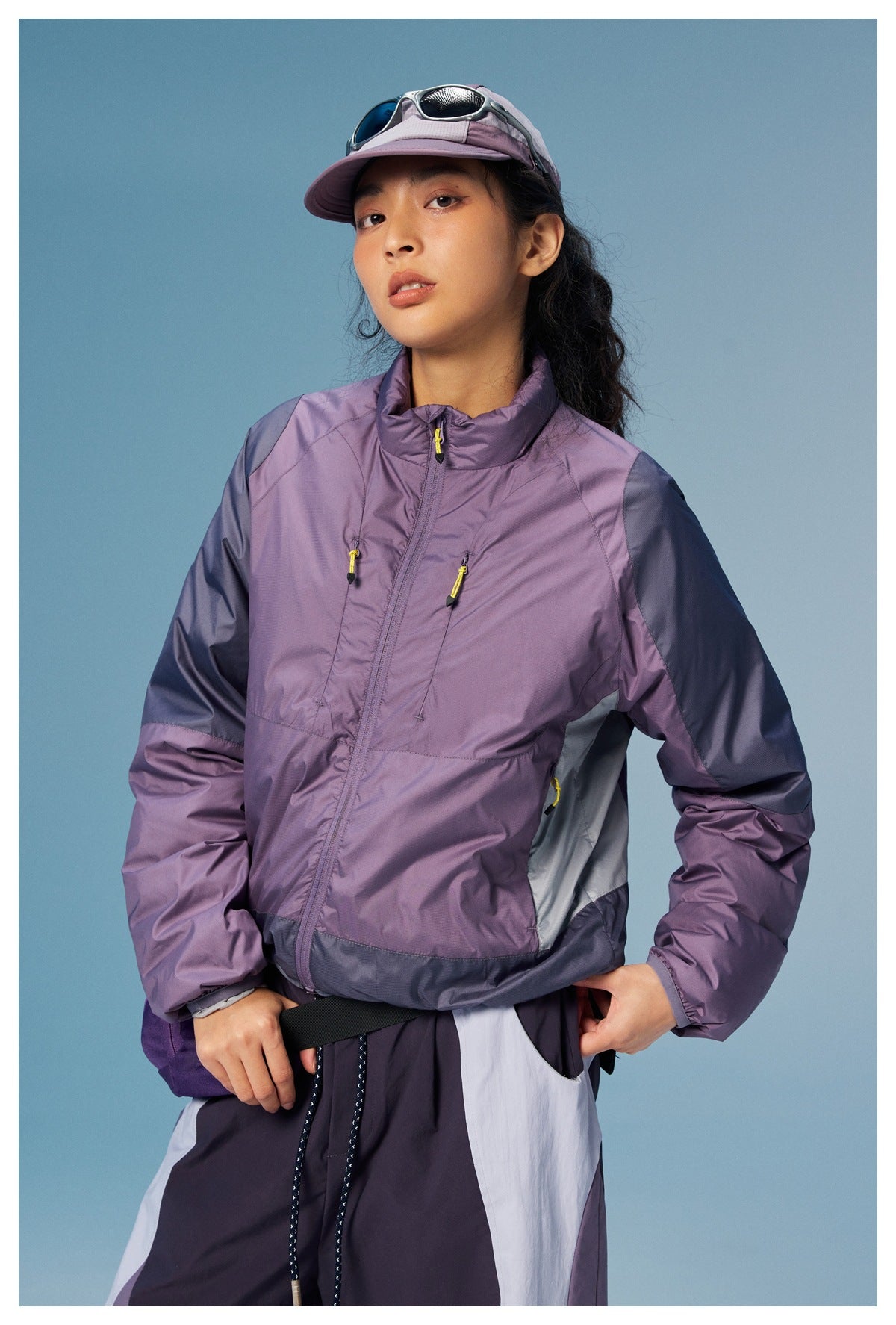 Front view of a model in a lavender color-block jacket with a high collar, zip pockets, and yellow zipper pulls.