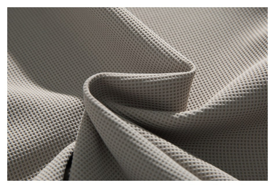 Close-up of light gray-beige fabric with a small, evenly spaced waffle-like texture, arranged in soft folds.