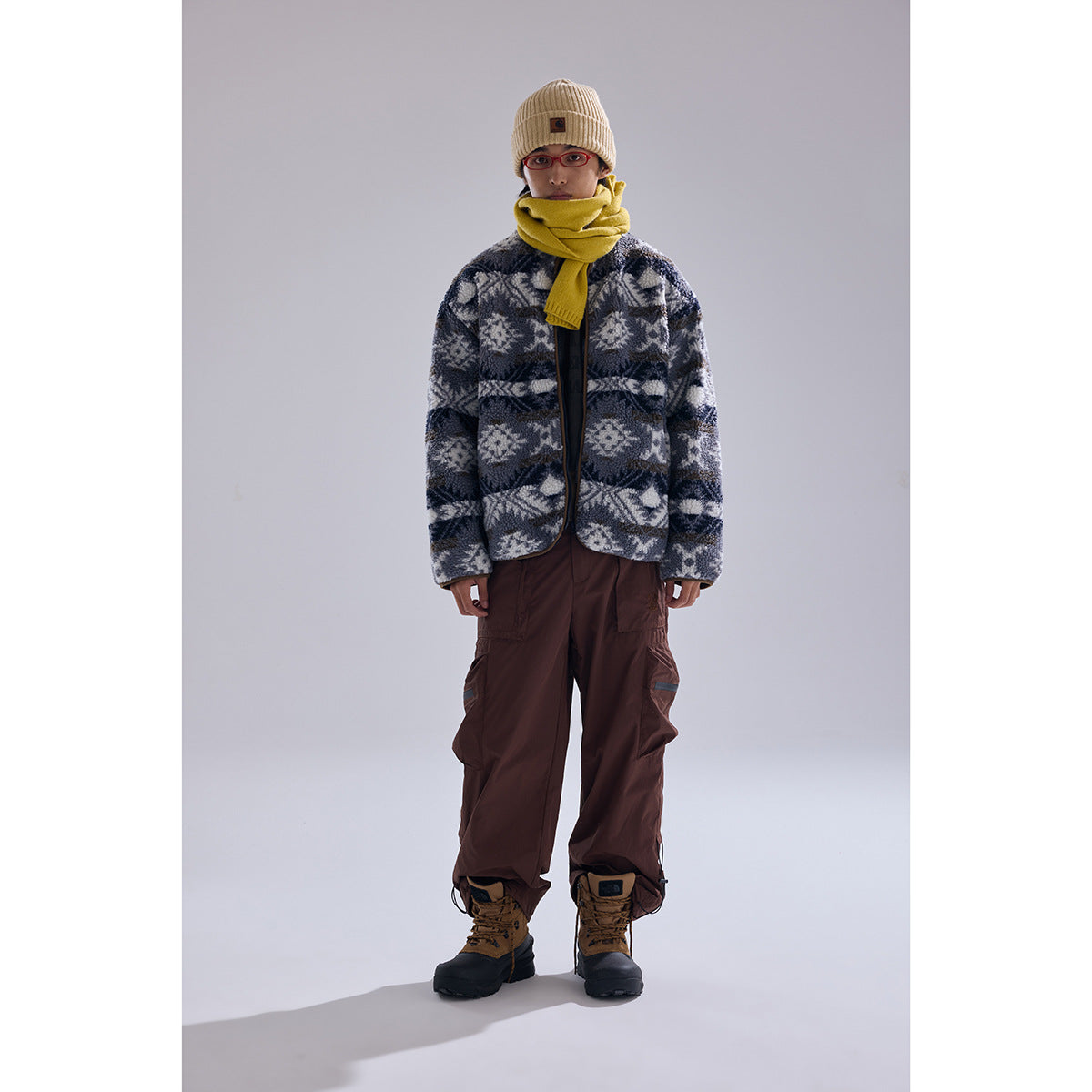 Full-length front view of a model wearing a gray patterned fleece jacket, yellow scarf, beige beanie, and brown cargo pants.