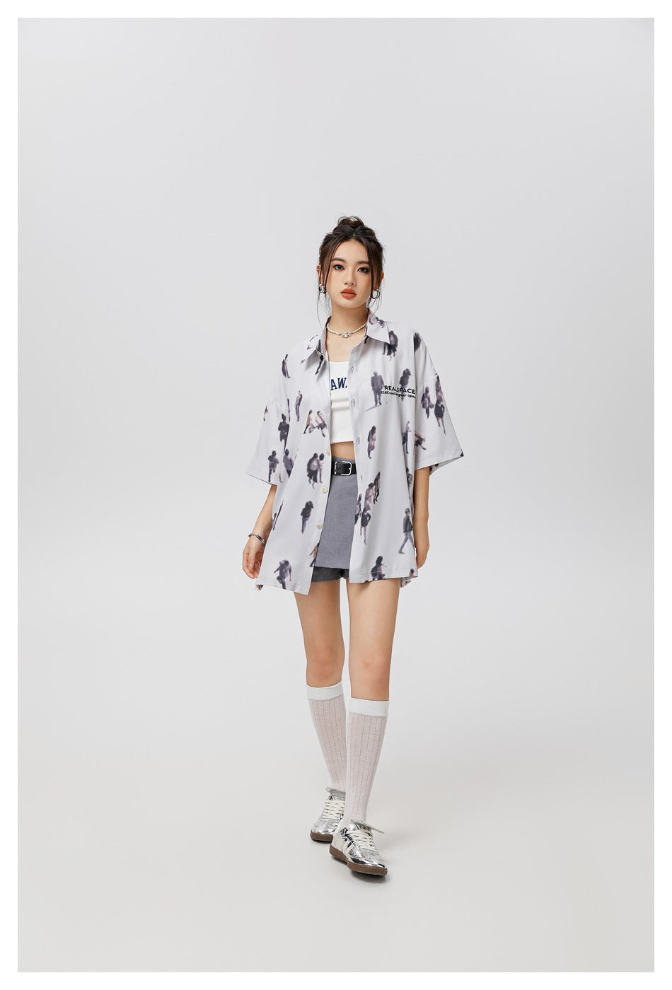 Full-length model wearing an oversized pale gray shirt with a scattered miniature-people print.