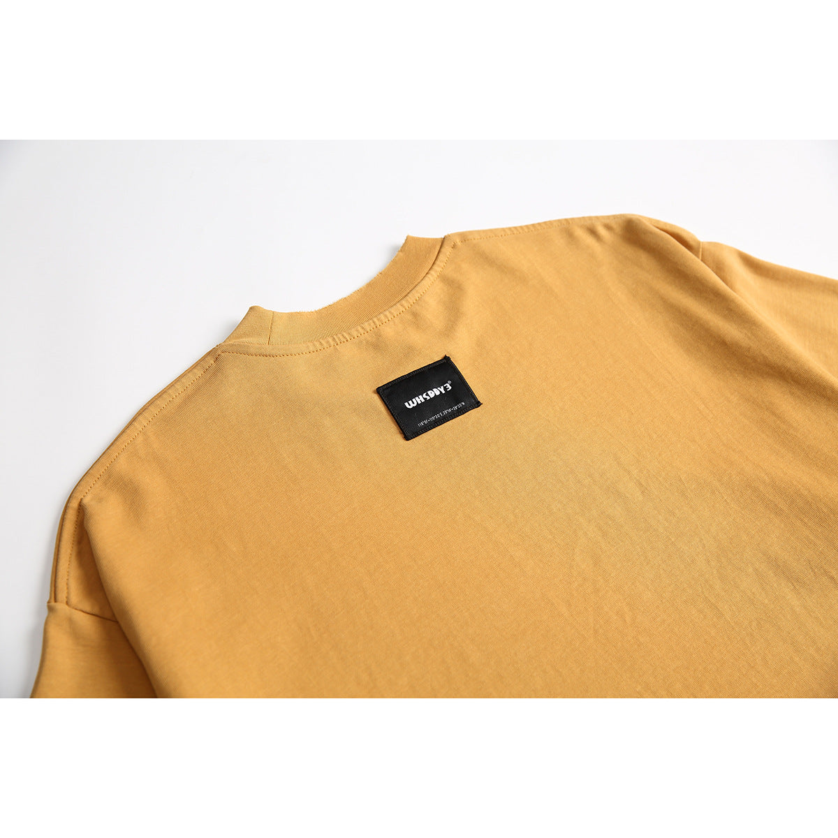 Close-up of the upper back and collar of a mustard T-shirt with a small black sewn label.