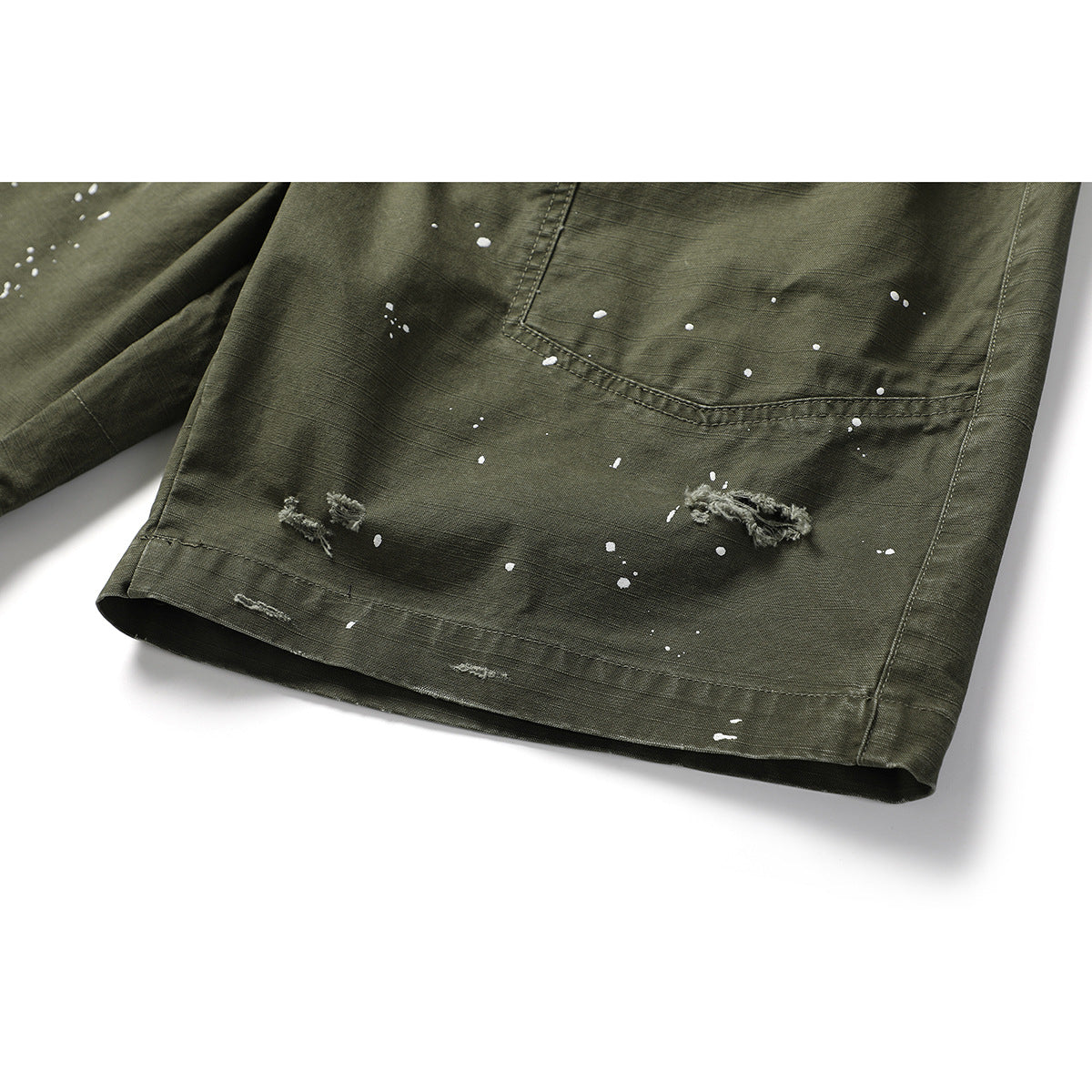 Close-up of olive shorts showing white paint-like splatters, distressed marks, stitching and the hem.