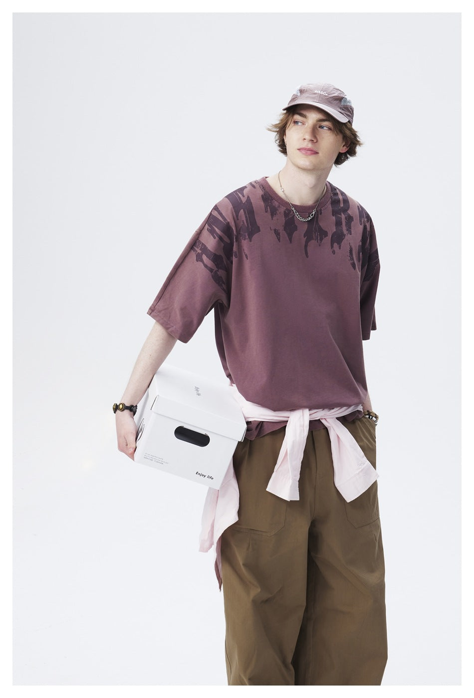 Model in a mauve oversized T-shirt with dark abstract shoulder graphics and olive cargo pants, framed from head to thighs.