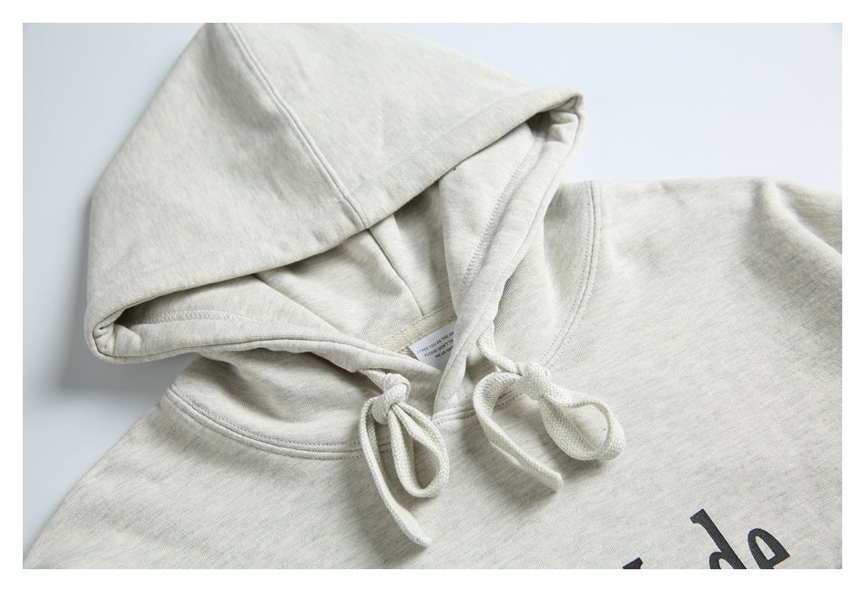 Close-up of a light gray hoodie’s hood, drawstrings, and partial black chest print.