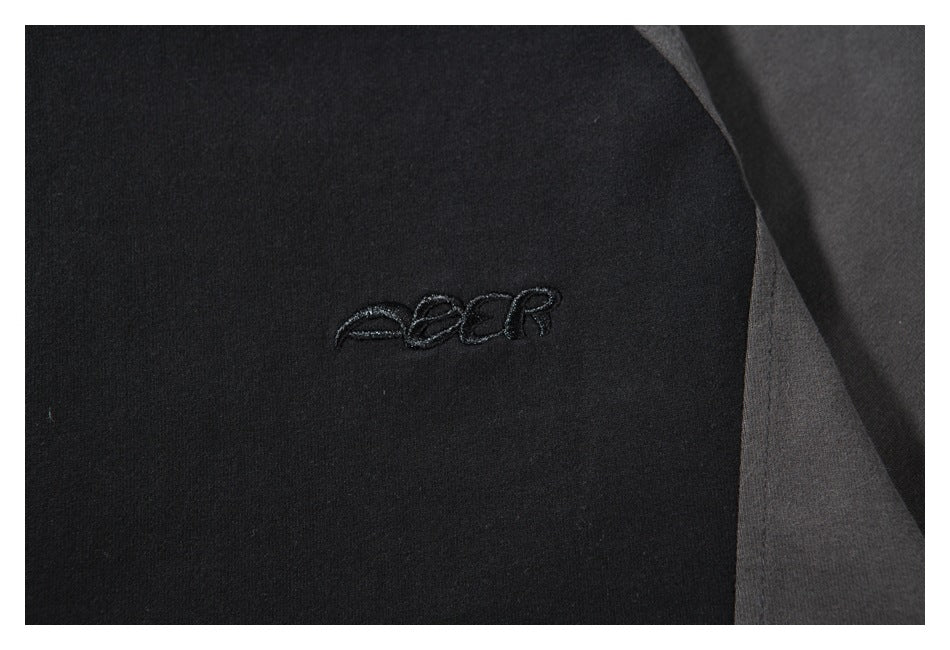 Close-up of a small dark embroidered logo on the black shirt, beside a charcoal gray panel.