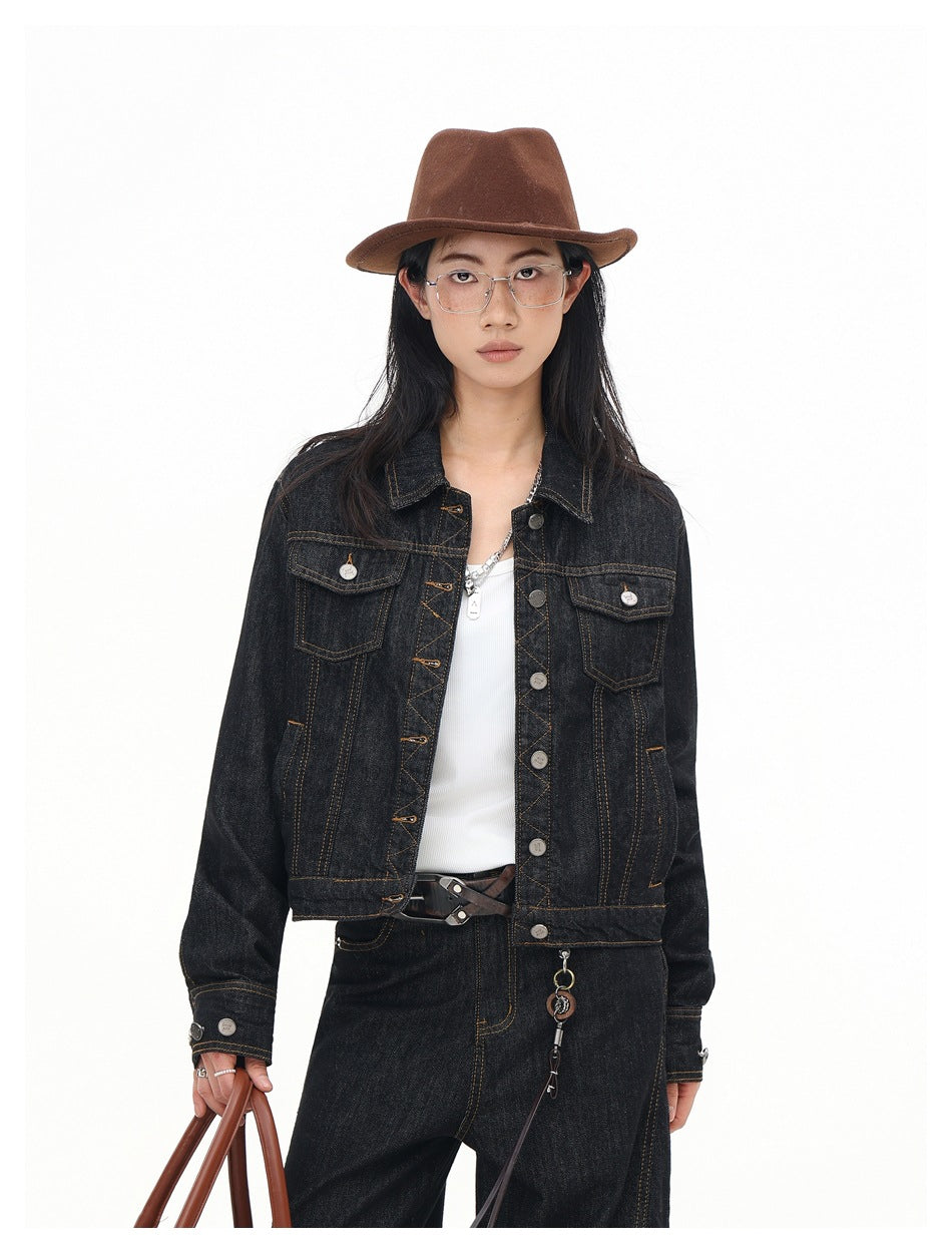 Closer view of a model wearing a dark indigo denim jacket with contrast stitching, metal buttons, and two flap chest pockets.
