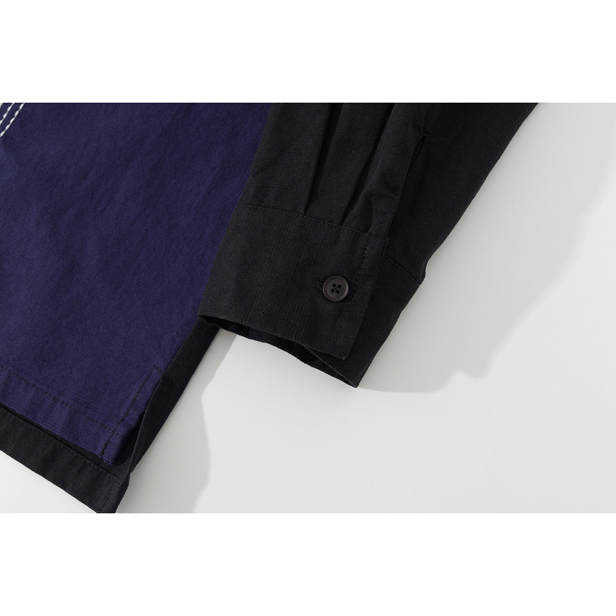 Close-up of a black shirt cuff beside a navy panel with white stitching and piping.