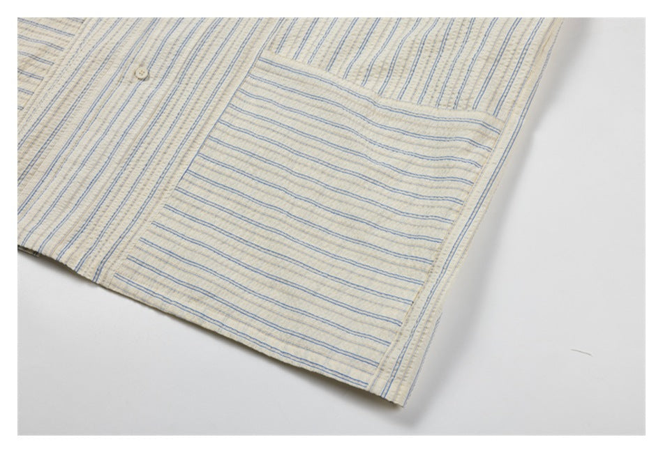 Close-up of a large chest pocket on a cream shirt with fine blue and tan stripes.