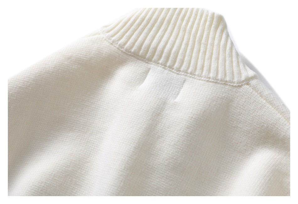 Close-up of the ribbed high collar and shoulder seam of an ivory knit sweater.