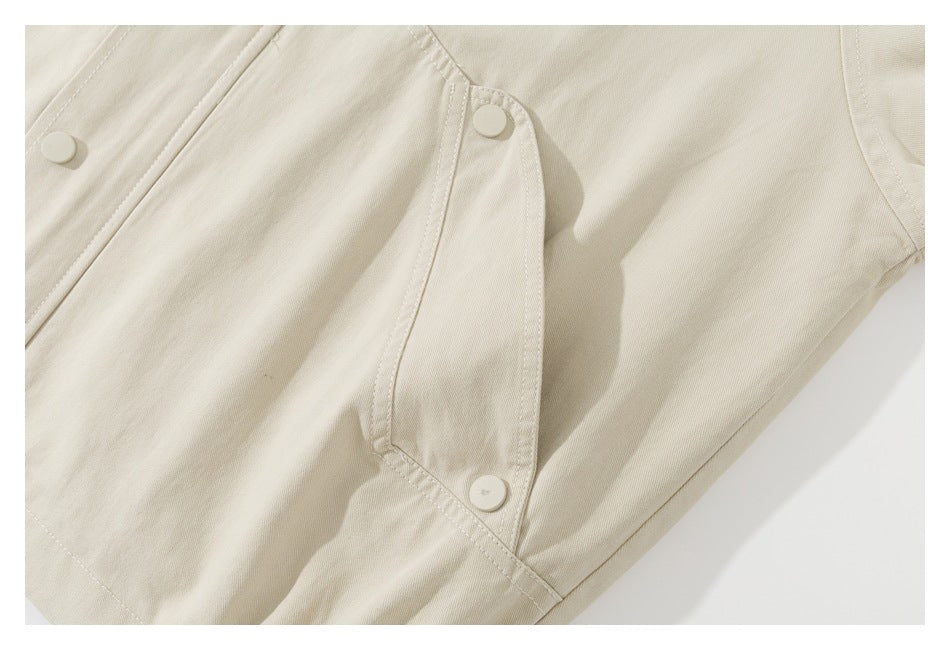 Close-up of a beige jacket's side panel with a snap-button tab and stitched seams.