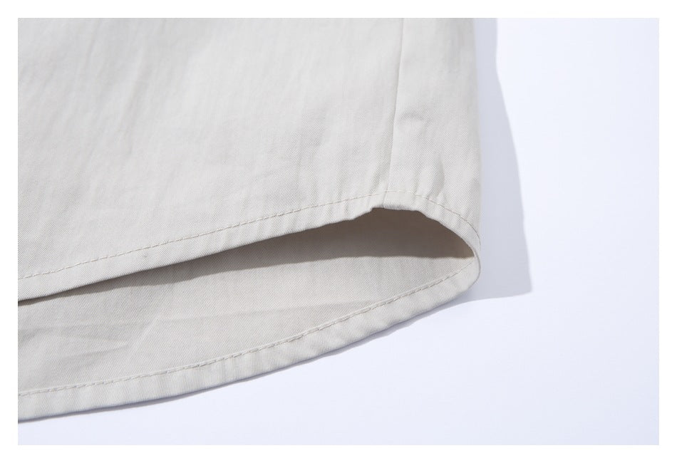 Close-up of the curved, double-stitched hem of a white shirt laid flat.