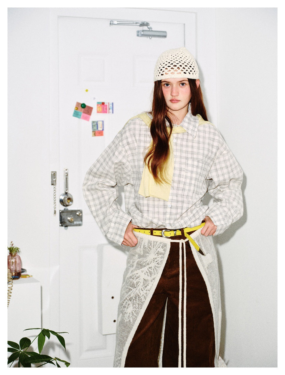 Model wearing the white checked shirt open over a yellow top, with a crochet cap, lace skirt and brown corduroy pants