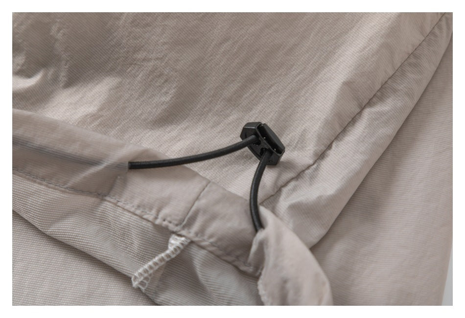 Close-up of a taupe garment's black elastic drawcord and toggle at a stitched edge.