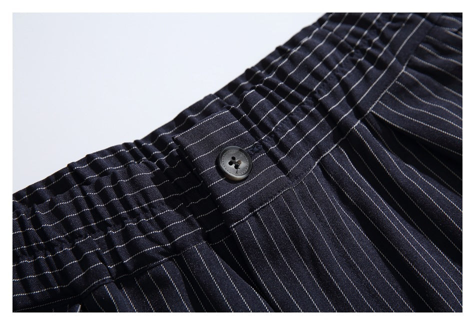 Close-up of dark pinstriped trousers showing the waistband button and front fastening area.