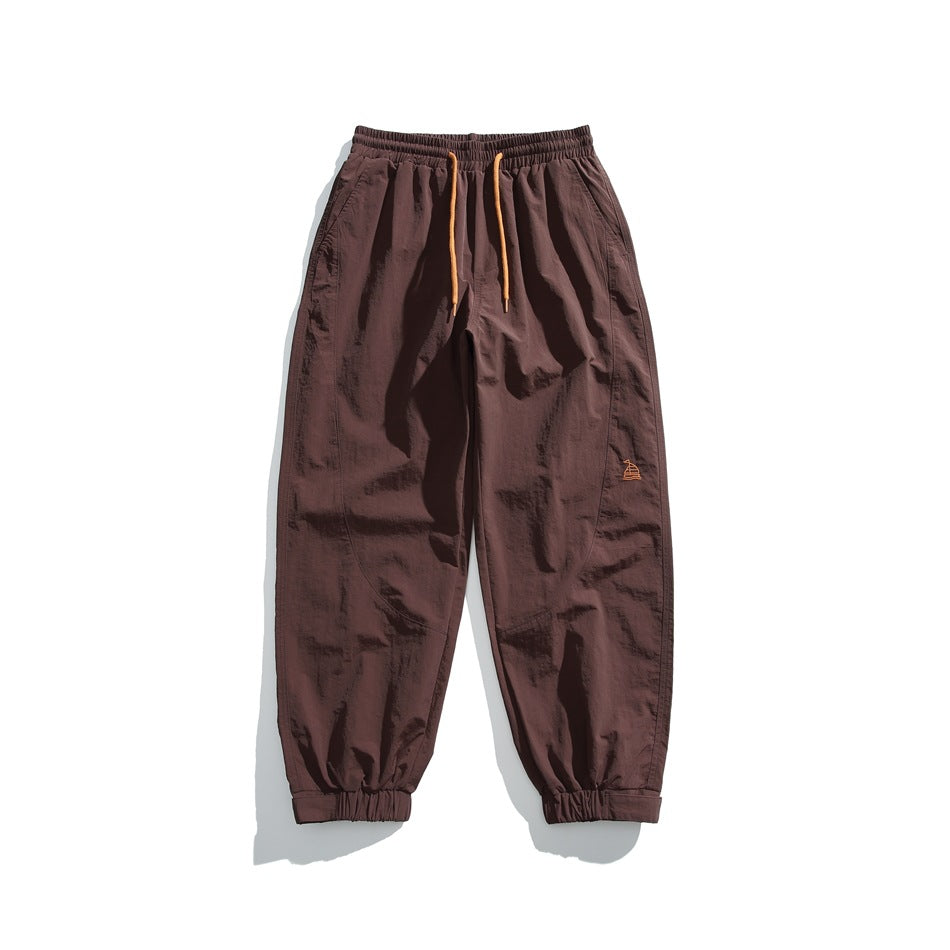 Brown jogger pants flat lay with orange drawstring, elastic cuffs and small embroidered logo