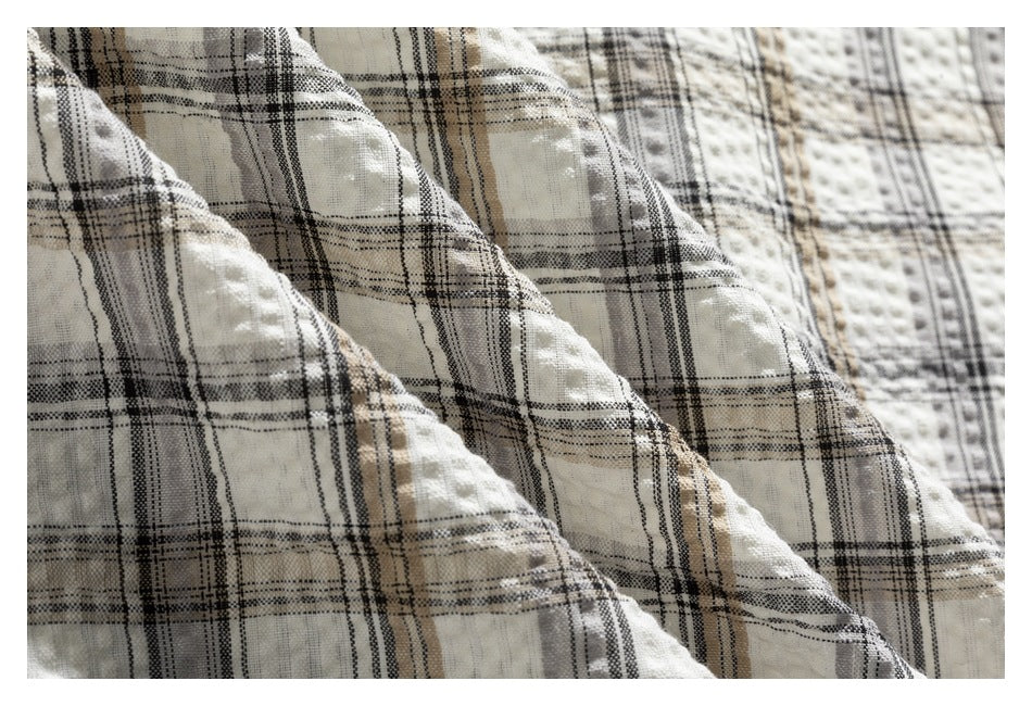 Close-up of layered cream fabric with a black and tan plaid pattern and raised texture.