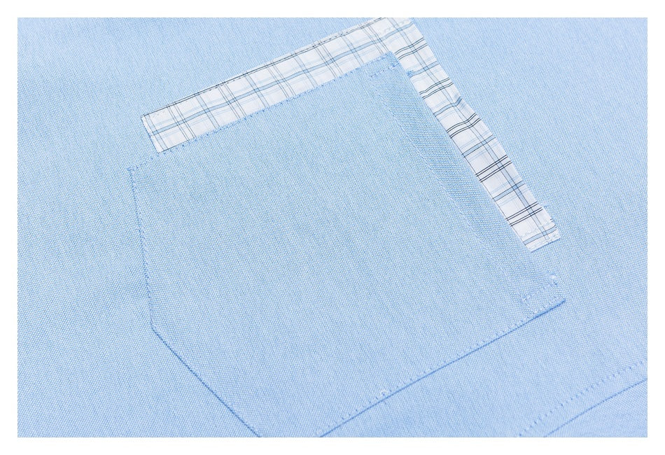 Close-up of a light blue shirt chest pocket with plaid trim along its upper and side edges.