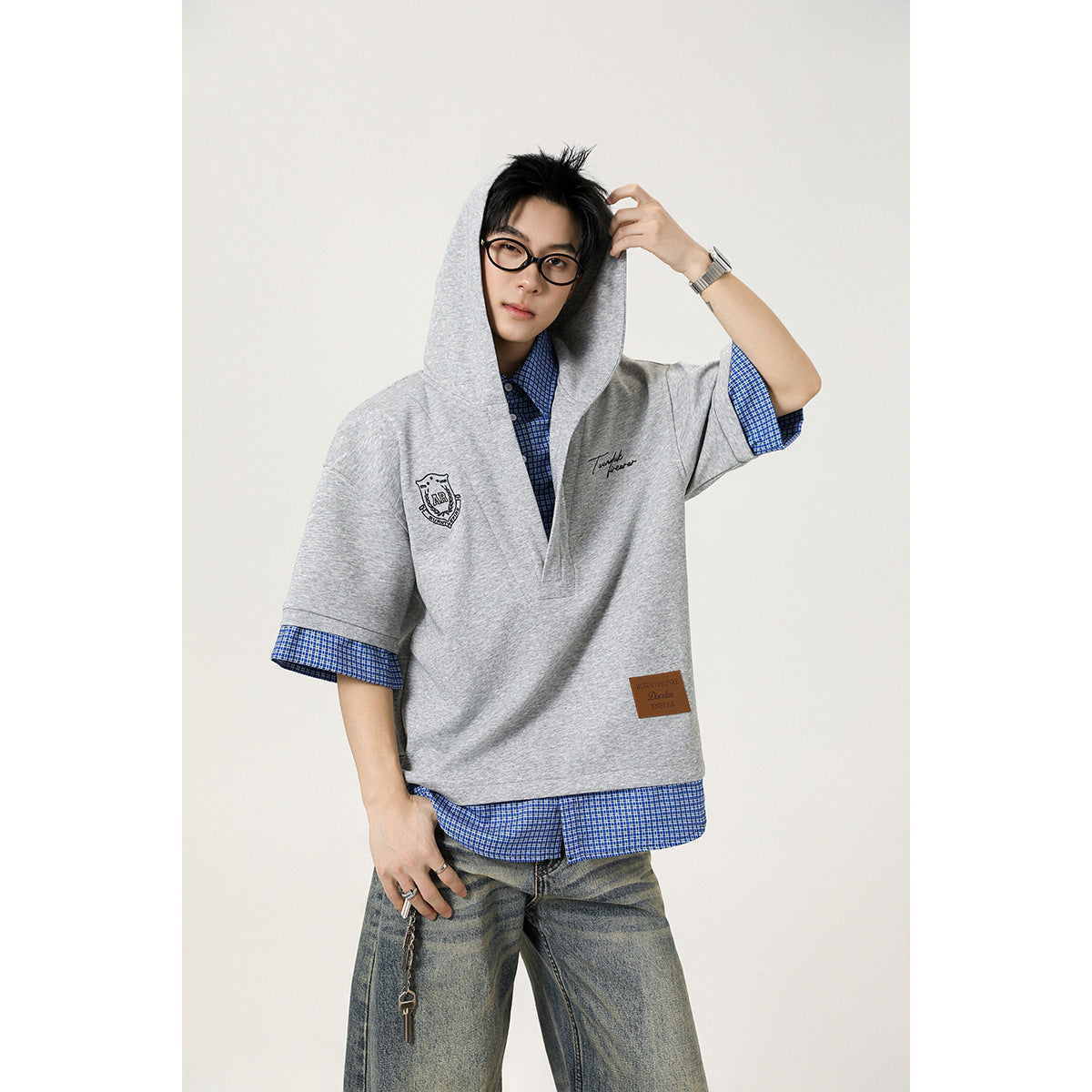Model wearing a light gray short-sleeve hooded pullover over a blue checked shirt.