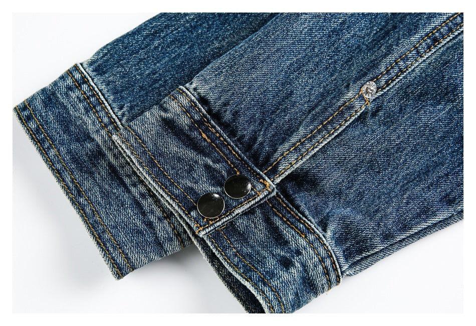 Close-up of a blue denim cuff with two dark snaps and orange stitching.