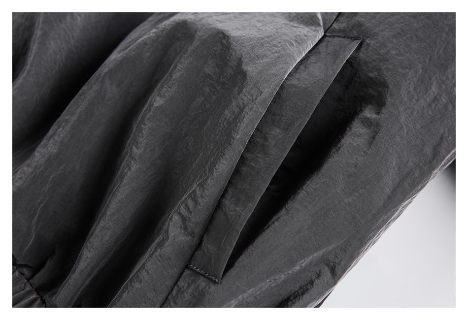 Close-up of dark charcoal garment fabric with a stitched pocket opening and overlapping panel.