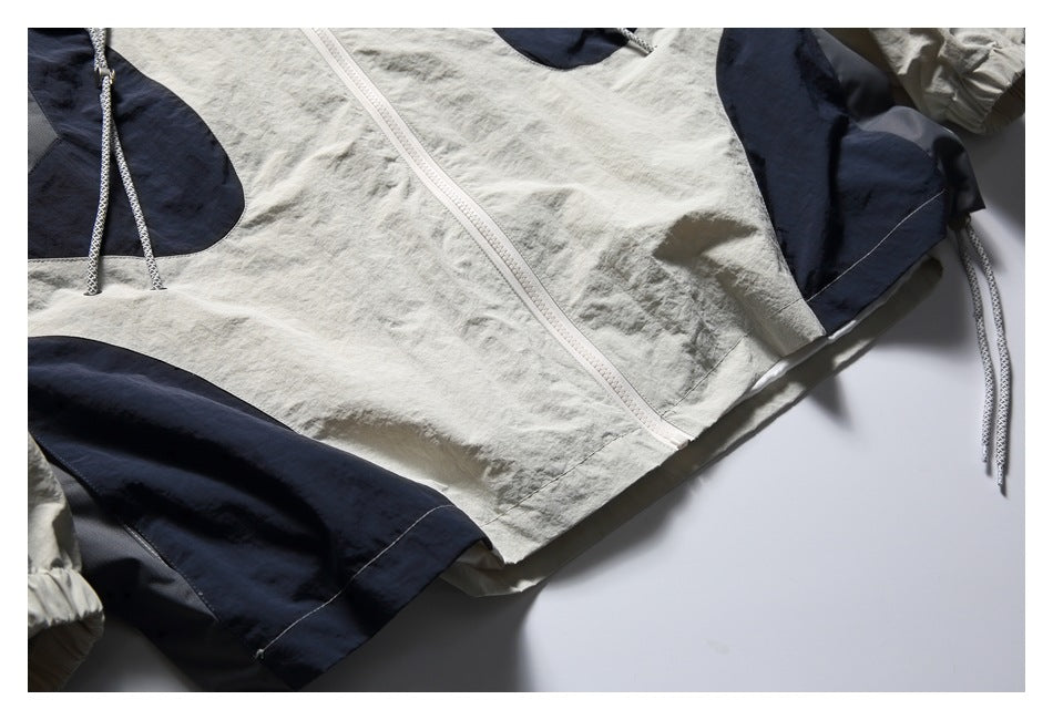 Close-up of the off-white jacket's lower front, white zipper, navy panels, and dangling side cord.