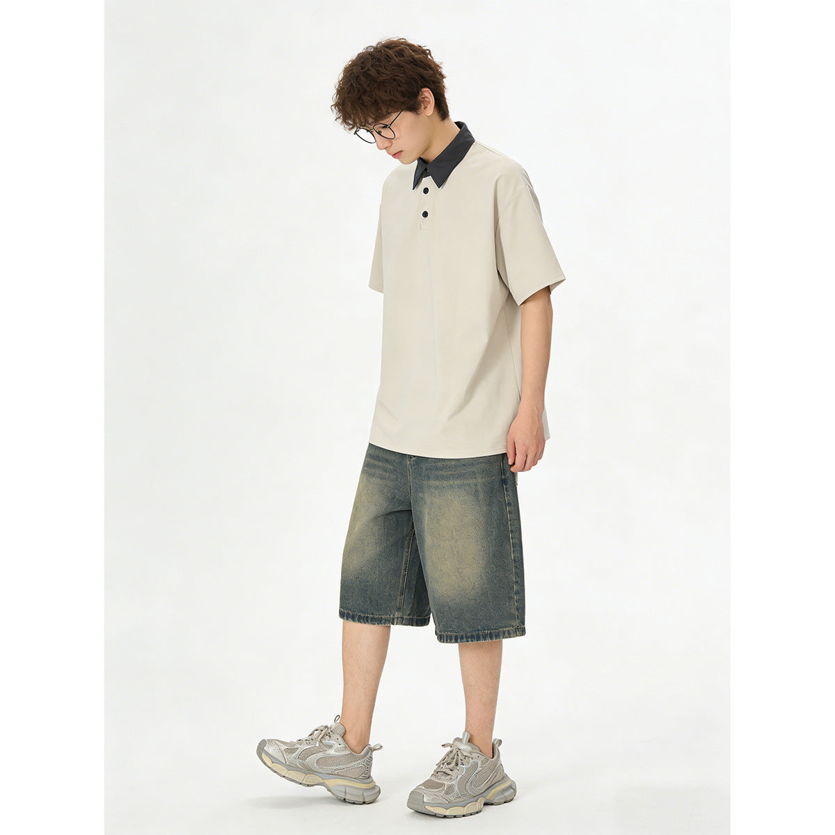 Model wearing a cream polo with black collar and buttons, faded denim shorts, and gray sneakers, shown from the front.