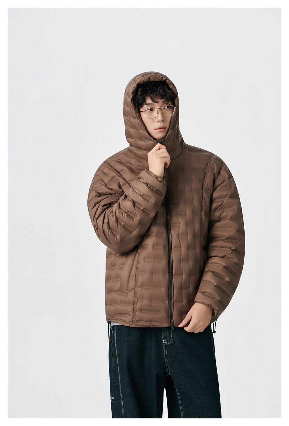 Model wearing a zipped brown quilted hooded jacket with the hood up and dark jeans.