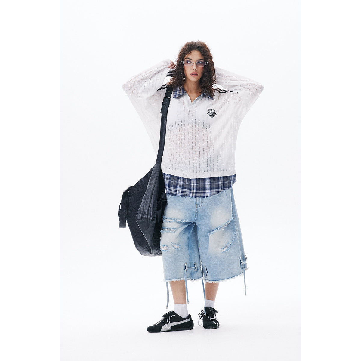 Model wearing a sheer white long-sleeve polo with a plaid collar, light denim shorts and a black shoulder bag.