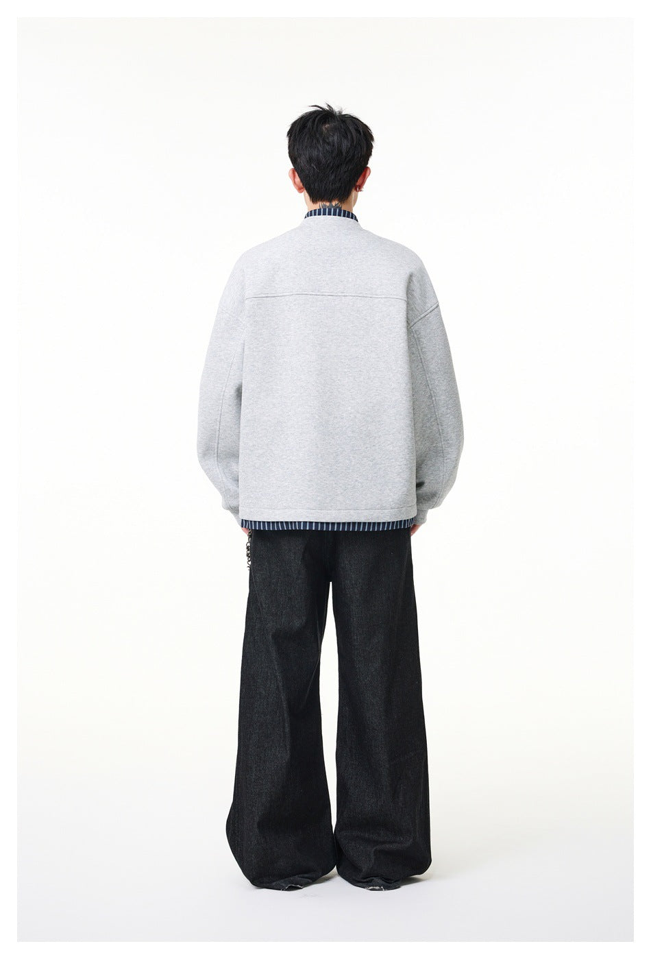 Back view of a model wearing a light gray jacket with striped trim and wide black trousers.
