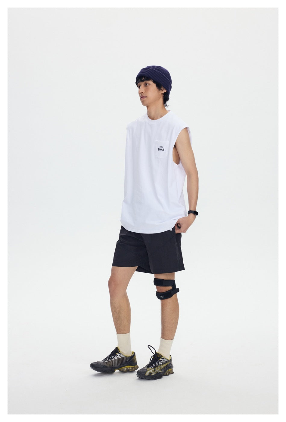 Full-length model wearing a white sleeveless pocket tee and black shorts in a white studio.