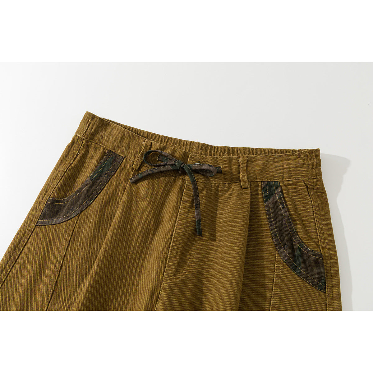 Close-up of mustard-brown shorts showing the drawstring waist and curved dark contrasting front pockets.
