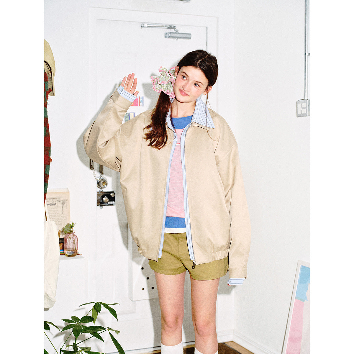Model wearing an open beige zip jacket with blue striped collar and cuffs, layered over a pink and blue top.