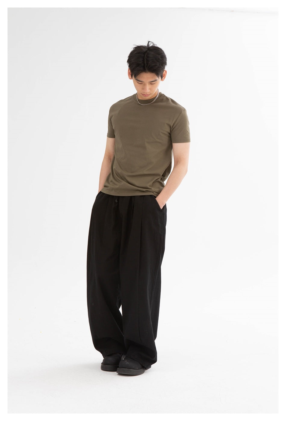 Full-length front view of a model wearing an olive-brown crew-neck T-shirt and loose black trousers.