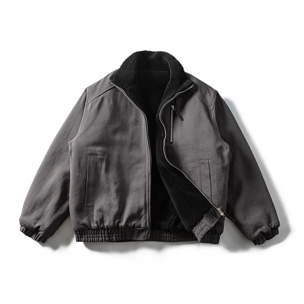 Dark gray bomber jacket laid flat and partly unzipped, showing the black fleece-like interior and collar