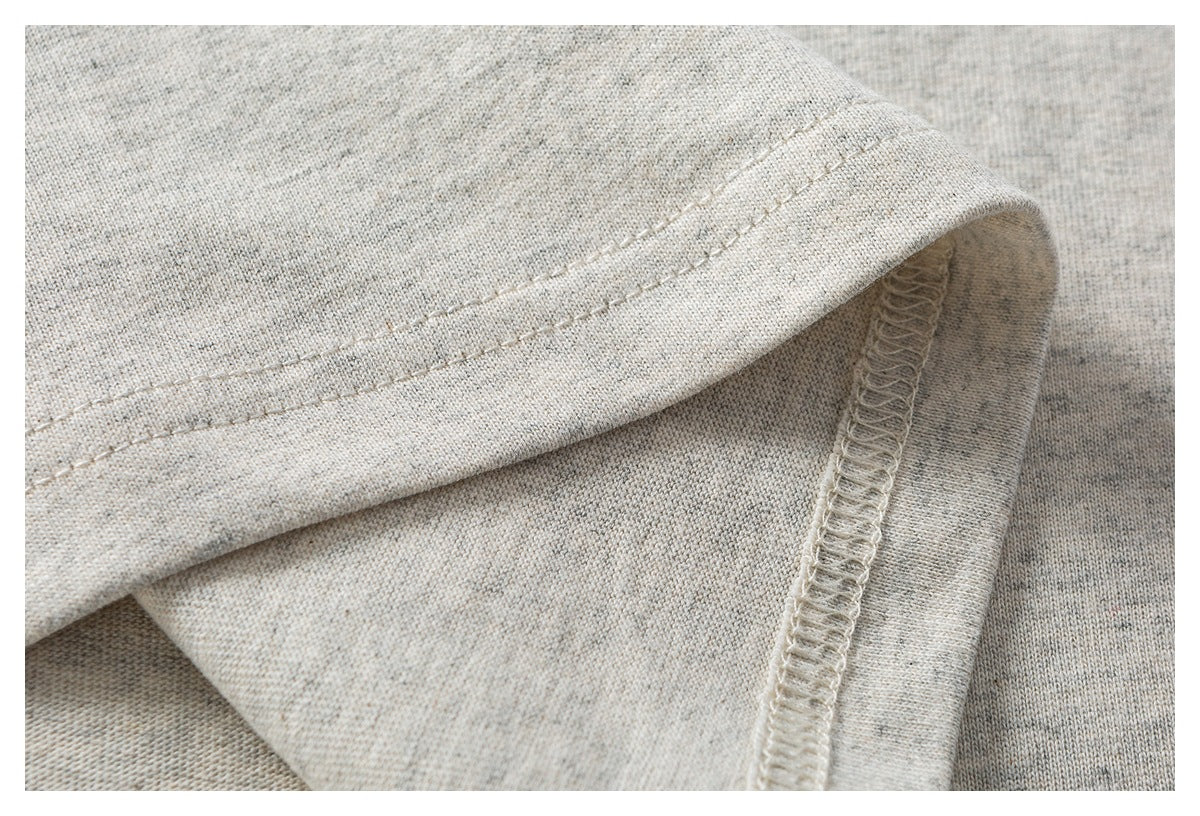 Close-up of a finished hem with visible topstitching and overlocked seam on light gray heathered fabric.