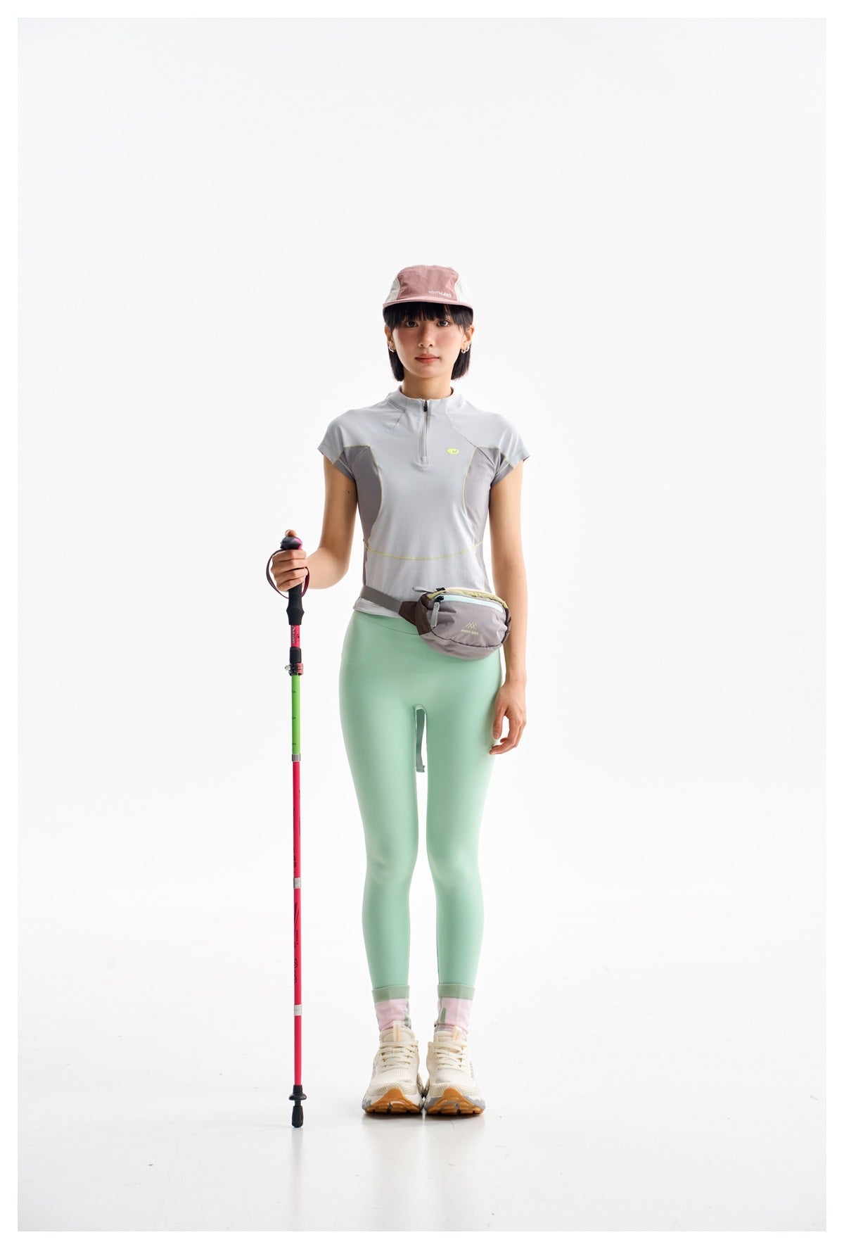 Full-length model wearing a light gray quarter-zip top, mint leggings, and a color-block cap.