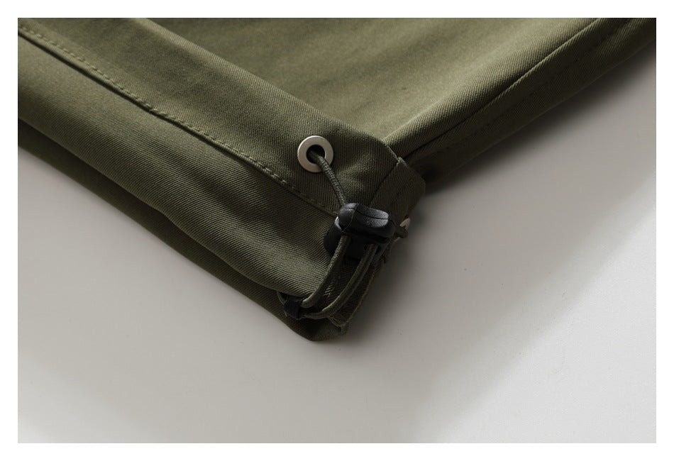 Close-up of an olive-green garment hem with a metal eyelet and black elastic drawcord toggle.